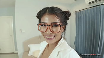 A bespectacled Thai woman with big tits gives a blowjob to her lover in front of the camera